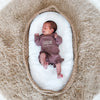 Newborn baby in a purple outfit with 'Alazae' name, lying on a white cushion surrounded by beige fabric.