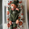 Baby in green outfit with 'James' on a pumpkin-patterned blanket